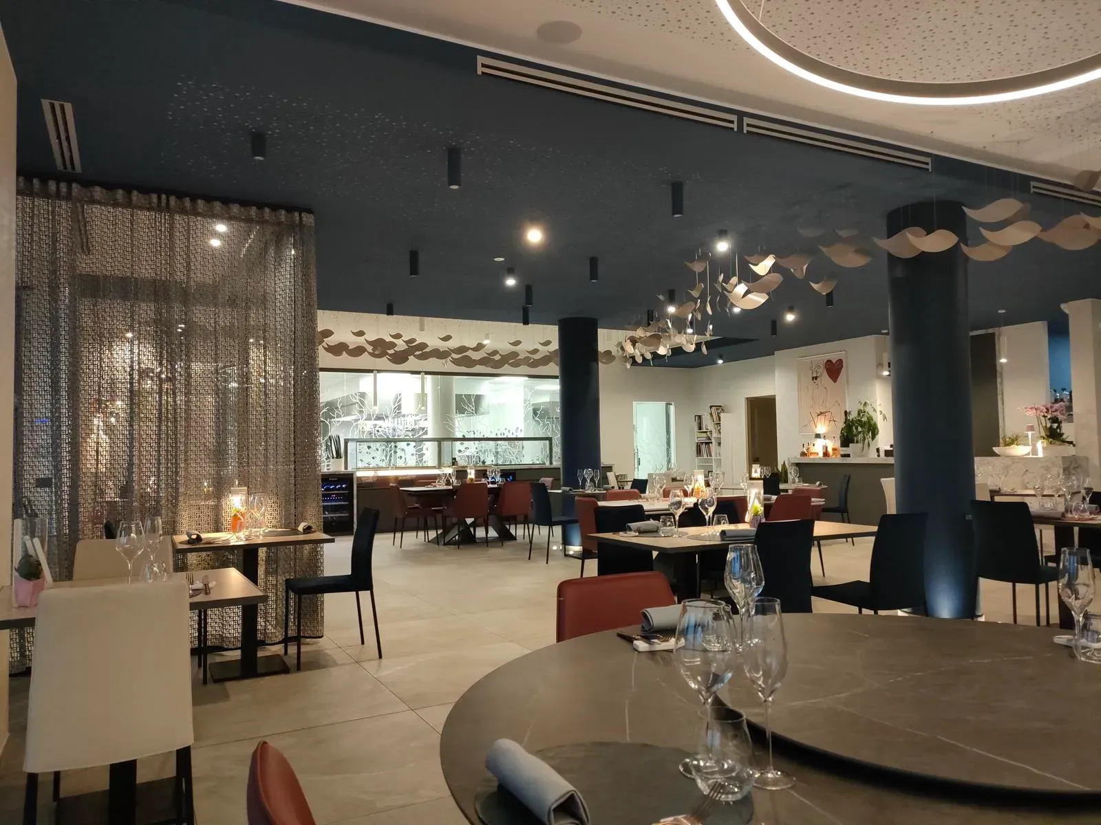 Sala interna di Costantino Crudo Re con colonne blu, decorazioni sospese a onda, tenda metallica e tavoli apparecchiati